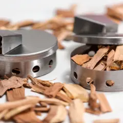 Dwa metalowe pojemniki zrębkami drewna, idealne do wędzenia ryb. Wybór odpowiedniego drewna, jakim drewnem wędzić ryby, nada im niepowtarzalny aromat.