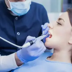 Dentysta w masce i rękawiczkach wykonuje zabieg. Zastanawiasz się, ile kosztuje znieczulenie u dentysty?