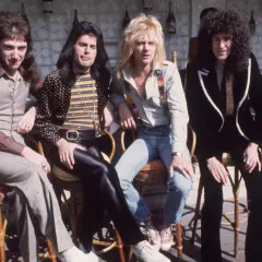 Freddie Mercury i zespół Queen siedzą przy barze w słoneczny dzień.