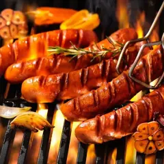 Aromatyczna kiełbasa z grilla skwierczy na ruszcie, otoczona płomieniami i przypieczonym czosnkiem.