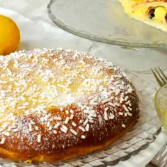 Una deliziosa polacca aversana, cosparsa di zucchero a velo e confettini, accanto a limoni freschi e una ciotola di crema pasticcera.