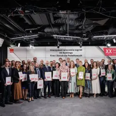 Grupa osób w garniturach i sukienkach pozuje do zdjęcia z nagrodami.