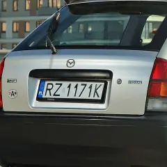 Srebrna Mazda 323 z tablicą rejestracyjną RZ 1171K.