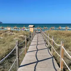 Holzsteg führt zu einem sonnigen Strand mit Strohschirmen bei Can Picafort. Ein Geheimtipp für entspannte Tage am Meer.