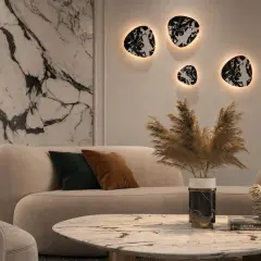 Nowoczesny salon z beżową sofą i marmurowym stolikiem. Na ścianie wiszą dekoracyjne kinkiety z kloszem, tworząc ciepłą atmosferę.