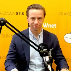 Krzysztof Bosak w garniturze przed mikrofonem na tle żółtej ściany z napisami.