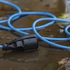 Niebieska przedłużka leży w kałuży, z wtyczką zanurzoną w wodzie.