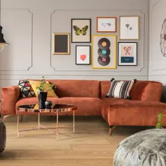 Pomarańczowa kanapa i stolik kawowy w stylu mid century modern. Na ścianie galeria obrazów z motywami retro.