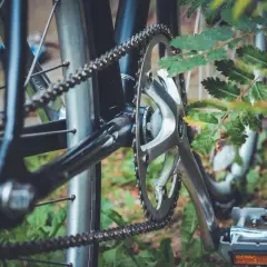 Jak dobrać łańcuch do roweru? Detal napędu: korba, zębatka i łańcuch rowerowy na tle zieleni.