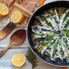 Alici in padella, pronte per essere gustate, con limone, erbe aromatiche e cipolla. Un piatto semplice e saporito.