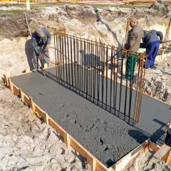 Budowa fundamentów: pracownicy wylewają beton na zbrojenie, tworząc solidny żelbeton.