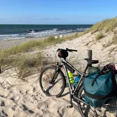 Rower z sakwami na plaży, gotowy do wyprawy rowerowej nad morzem. Słońce, piasek i szum fal.