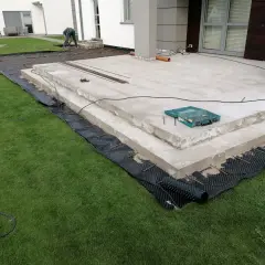 Budowa tarasu z betonu. Pracownicy przygotowują teren pod nową nawierzchnię, układając zbrojenie i materiały izolacyjne.