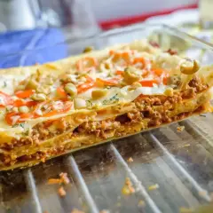 Pyszne, domowe piec lasagne z warstwami mięsa mielonego, makaronu i sera, ozdobione pomidorami i oliwkami.