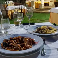 Dwa talerze z makaronem i owocami morza, kieliszki z winem i woda na stole w restauracji pod gołym niebem.