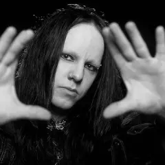 Joey Jordison, perkusista zespołu Slipknot, z rękami przed twarzą, w czerni i bieli.