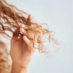 Mano acariciando cabello rizado, mostrando cómo rizar el pelo con espuma para definir ondas.