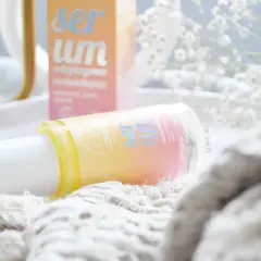Butelka serum rozświetlającego OnlyBio na białej tacy, obok pudełka i białych kwiatów.