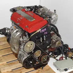 Silnik Honda VTEC z czerwonymi pokrywami zaworów, na drewnianej palecie.