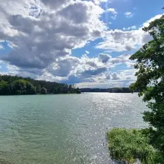 Spokojne jezioro na Kaszubach, otoczone lasem, z chmurami na niebie. To jak brama kaszubska do natury.