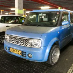 Niebieski Nissan Cube z tablicą rejestracyjną N193-701 W zaparkowany obok białego Volkswagena.