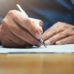 Main tenant rédigeant une lettre, peut-être un modèle lettre CARSAT, avec un stylo argenté sur un document.