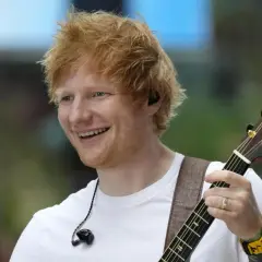 Ed Sheeran uśmiecha się, grając na gitarze podczas koncertu w Polsce.