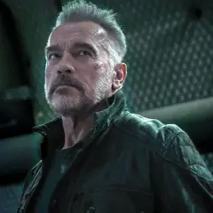 Arnold Schwarzenegger jako T-800 w filmach Jamesa Camerona. Z blizną na policzku, w skórzanej kurtce, patrzy w górę.