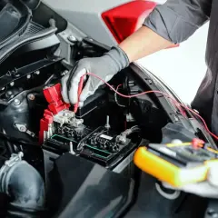 Mechanik w rękawiczkach sprawdza akumulator miernikiem, pokazując, jak sprawdzić alternator miernikiem.