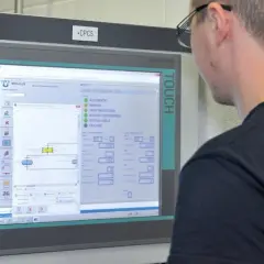 Mann vor Bedienfeld, das Lager Kennzahlen anzeigt. Software zeigt Status und Werte für Krane.