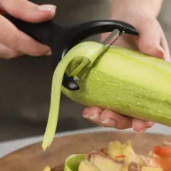 Une personne épluche une courgette. Les épluchures tombent sur une planche à découper, prêtes à être données aux poules.