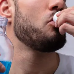 Uomo usa collutorio per parodontite, tenendo una bottiglia di liquido blu.