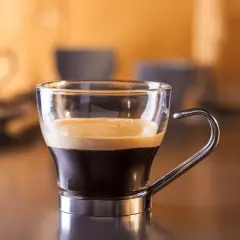 Kawa ristretto w szklanej filiżance z metalowym uchem. Kremowa pianka na ciemnym espresso.
