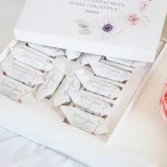 Otwarty biały kartonik z czekoladkami w ozdobnych papierkach, z motywem kwiatowym.