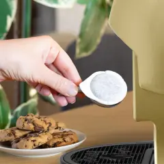 Una mano inserisce una cialda ese, perfetta per un caffè veloce, accanto a biscotti al cioccolato.