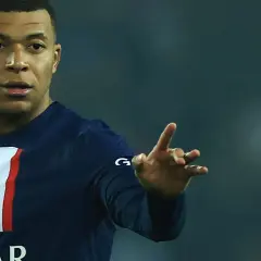 Kylian Mbappé w koszulce PSG, gdzie gra, pokazuje gest dłonią.