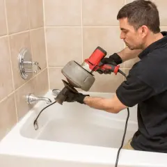 Plombier utilise un furet électrique pour comment déboucher une canalisation dans une baignoire.