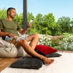 Homme assis, appliquant des électrodes sur sa cuisse, appareil de stimulation en main. Il observe le paysage fleuri, sans effets secondaires apparents du urostim.
