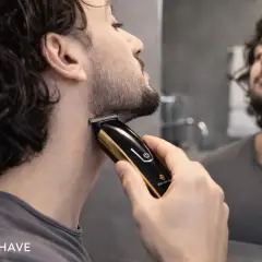 Un homme ajuste sa barbe 3mm avec une tondeuse dorée et noire devant un miroir.