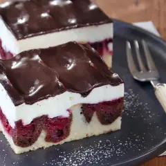 Zwei Stücke saftige Donauwelle mit Kirschen, weißer Creme und Schokoladenguss auf einem Teller. Ein köstliches Donauwelle Rezept!