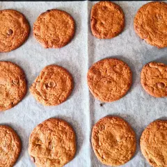 Tolv nybakade chocolate chip cookies ligger på ett bakplåtspapper. De är gyllene och ser härligt sega ut.