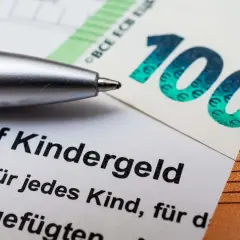Długopis nad dokumentem o Kindergeld w Niemczech, obok banknotów 100 i 50 euro.
