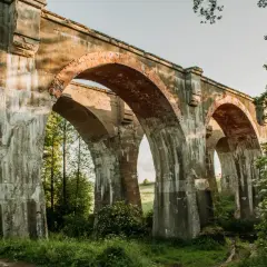 Imponujące, stare mosty w Kiepojciach, porośnięte zielenią, stoją dumnie pod błękitnym niebem.