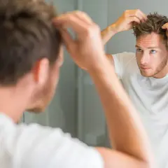 Ein Mann mit strohigem Haar stylt sich vor dem Spiegel.