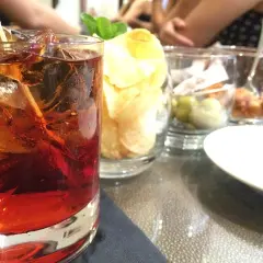 Czerwony drink z lodem i cytryną, obok chipsy i oliwki. Idealny na letnie wieczory, jak z przepisu na absynt.