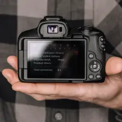 Dłoń trzyma aparat, na ekranie menu. Minimalizm w fotografii to sztuka uchwycenia esencji.
