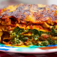 Porción de lasaña de verduras, con capas de pasta, espinacas y salsa roja, servida en un plato colorido.
