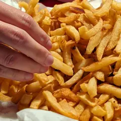 En hand plockar en gyllene pommes frites ur en stor hög med krispiga pommes frites.