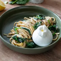 Zitronen Pasta mit Spinat und Burrata auf einem grünen Teller, daneben eine Zitronenhälfte.