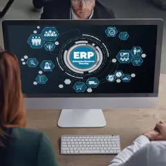 Zespół analizuje diagram ERP na ekranie komputera. Ikony symbolizują różne moduły systemu, od zarządzania zasobami ludzkimi po logistykę.